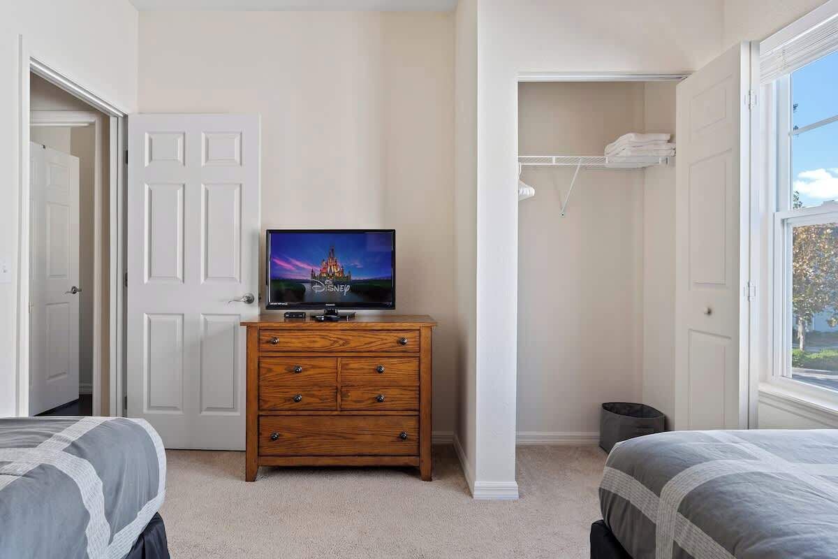 A bedroom with a TV on a dresser, a closet, and a window with a view.