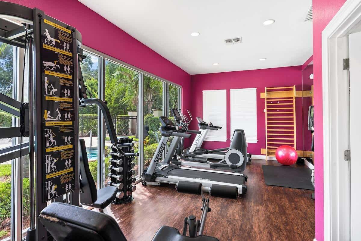 A gym with exercise equipment, large windows, and a view of greenery outside.