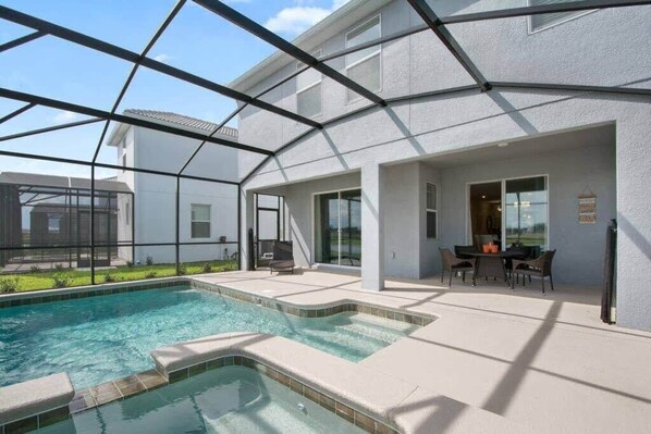 A swimming pool with a glass enclosure, a patio area with outdoor furniture, and a building with large windows. - Stunning Home, Private Pool, Great Location (Kissimmee)