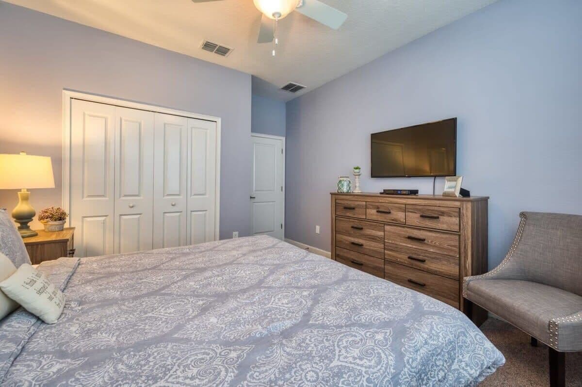 A bedroom with a bed, a dresser, a chair, a television, and a ceiling fan.