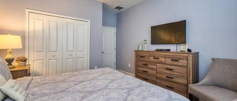 A bedroom with a bed, a dresser, a chair, a television, and a ceiling fan.