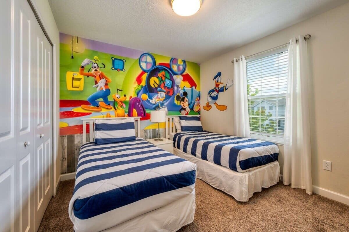 A bedroom with two beds, a colorful mural, and a window with curtains.