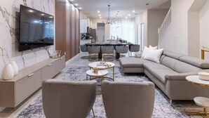 A modern living room with a large TV, a sectional sofa, and a dining area with a table and chairs. - Themed Luxury 5br, Best Family Getaway (Clermont)