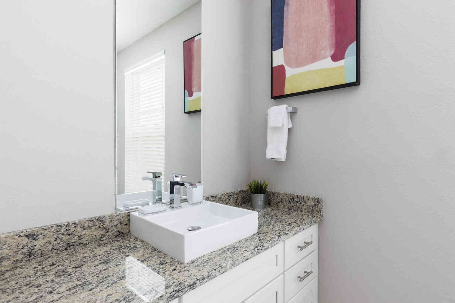 A modern bathroom with a white sink, granite countertop, and a large mirror.