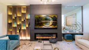 Ein modernes Wohnzimmer mit Kamin, einem großen, darüber montierten Fernseher und einem dekorativen Regal mit verschiedenen Gegenständen.