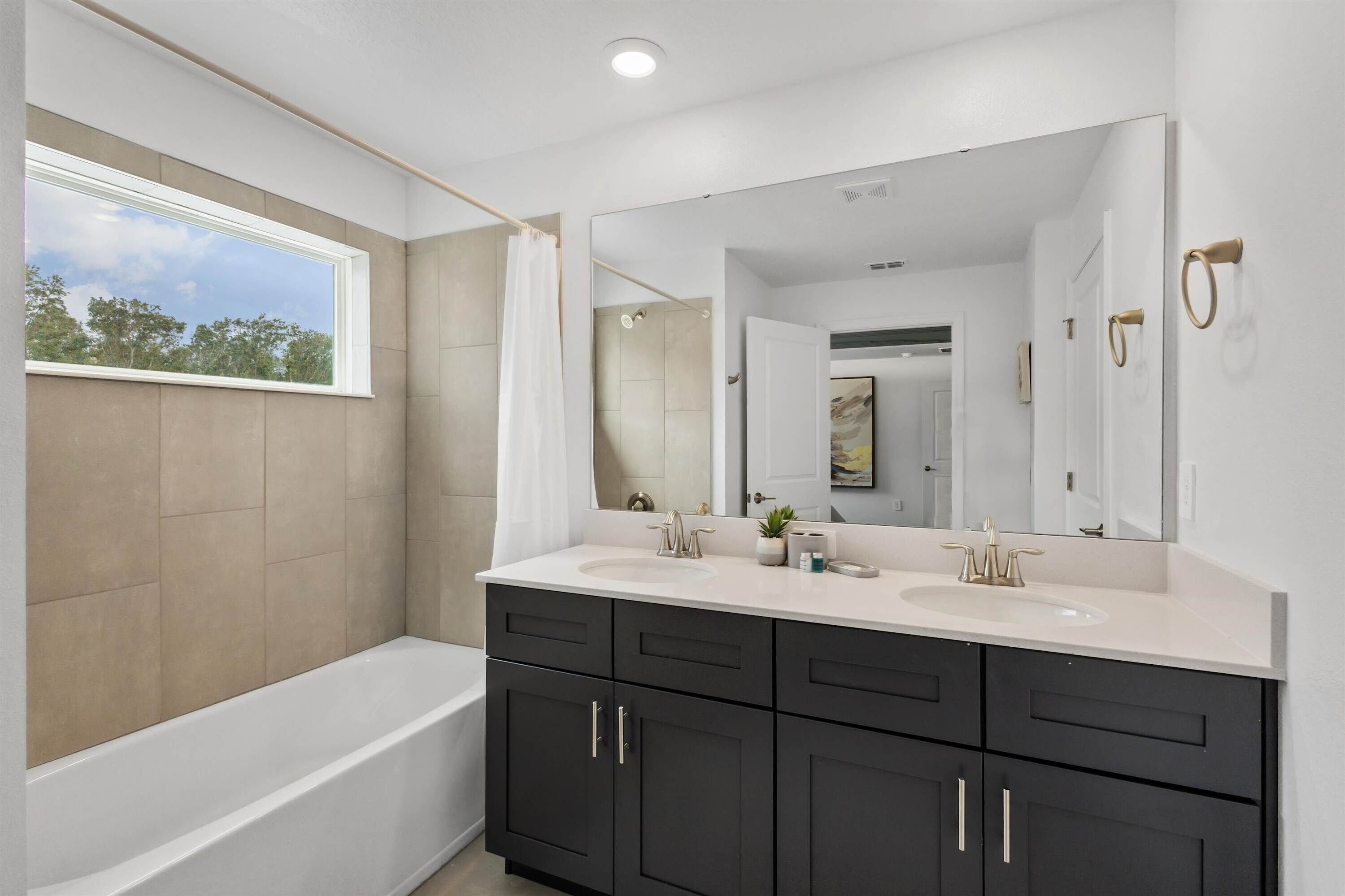 A modern bathroom with a bathtub, two sinks, dark cabinets, and a large mirror.