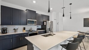A modern kitchen with dark cabinets, a large island, stainless steel appliances, and pendant lighting. - Stylish Family Retreat With Themed Bedrooms (Kissimmee)