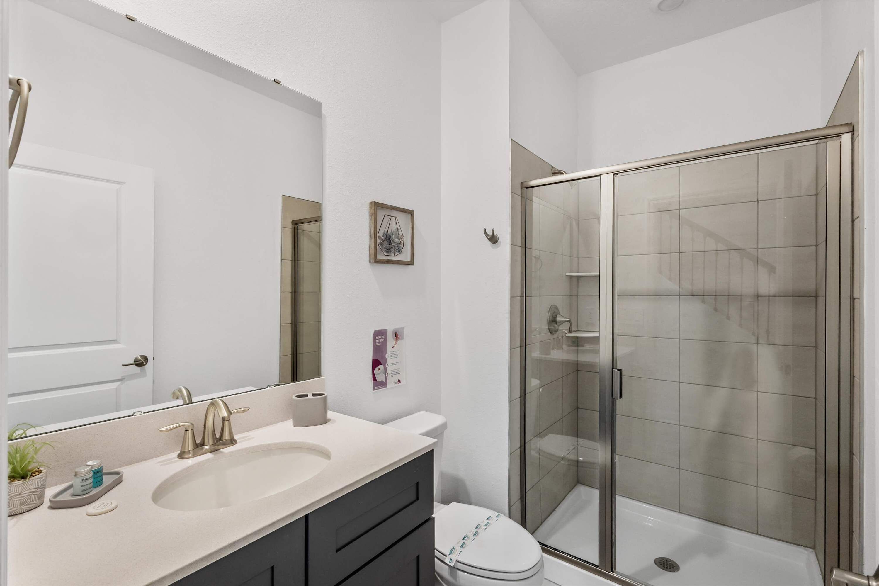 Un baño con lavamanos, espejo, inodoro y ducha con mampara de vidrio.