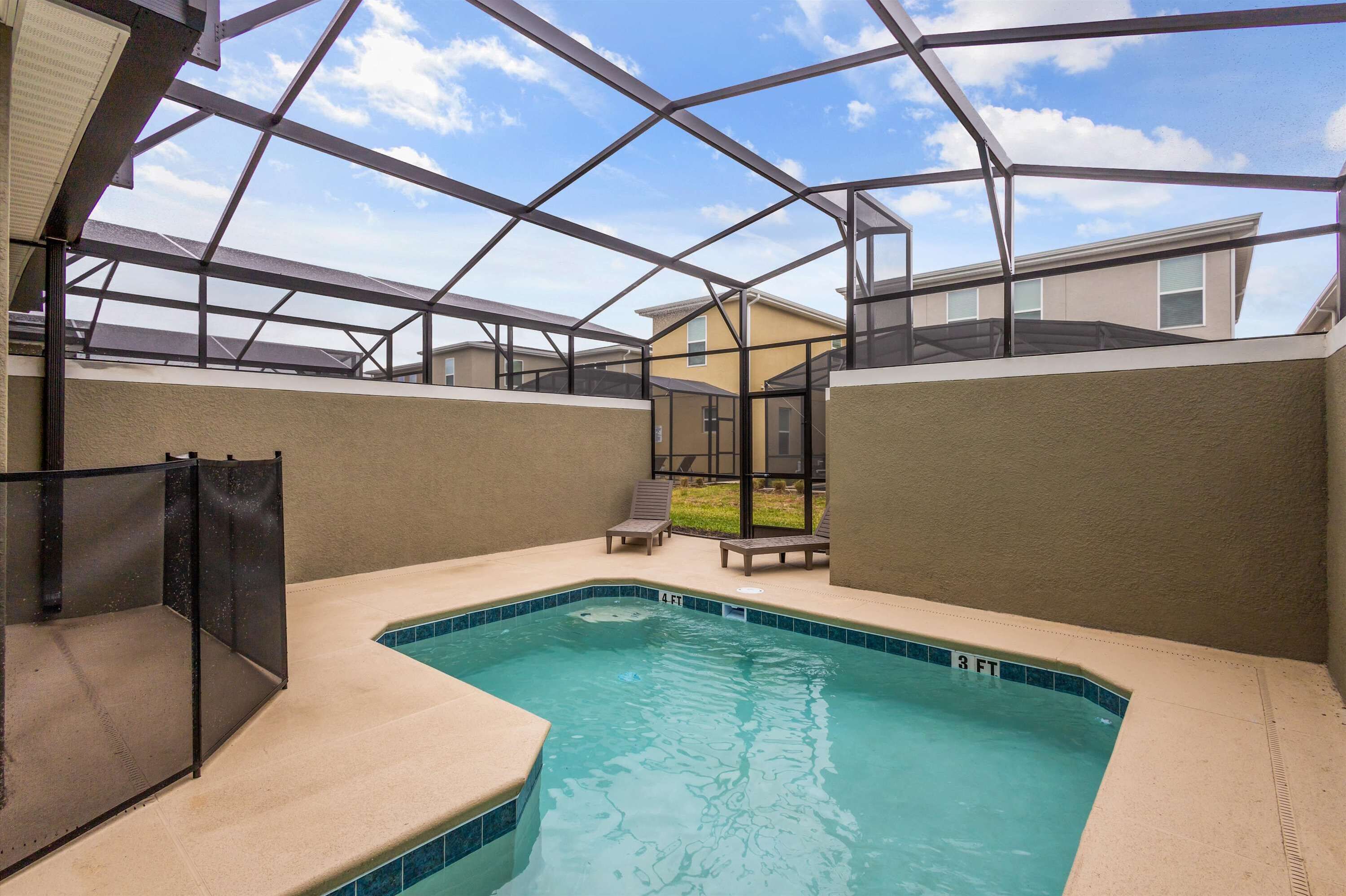 A swimming pool with a glass ceiling, surrounded by lounge chairs and a view of houses.