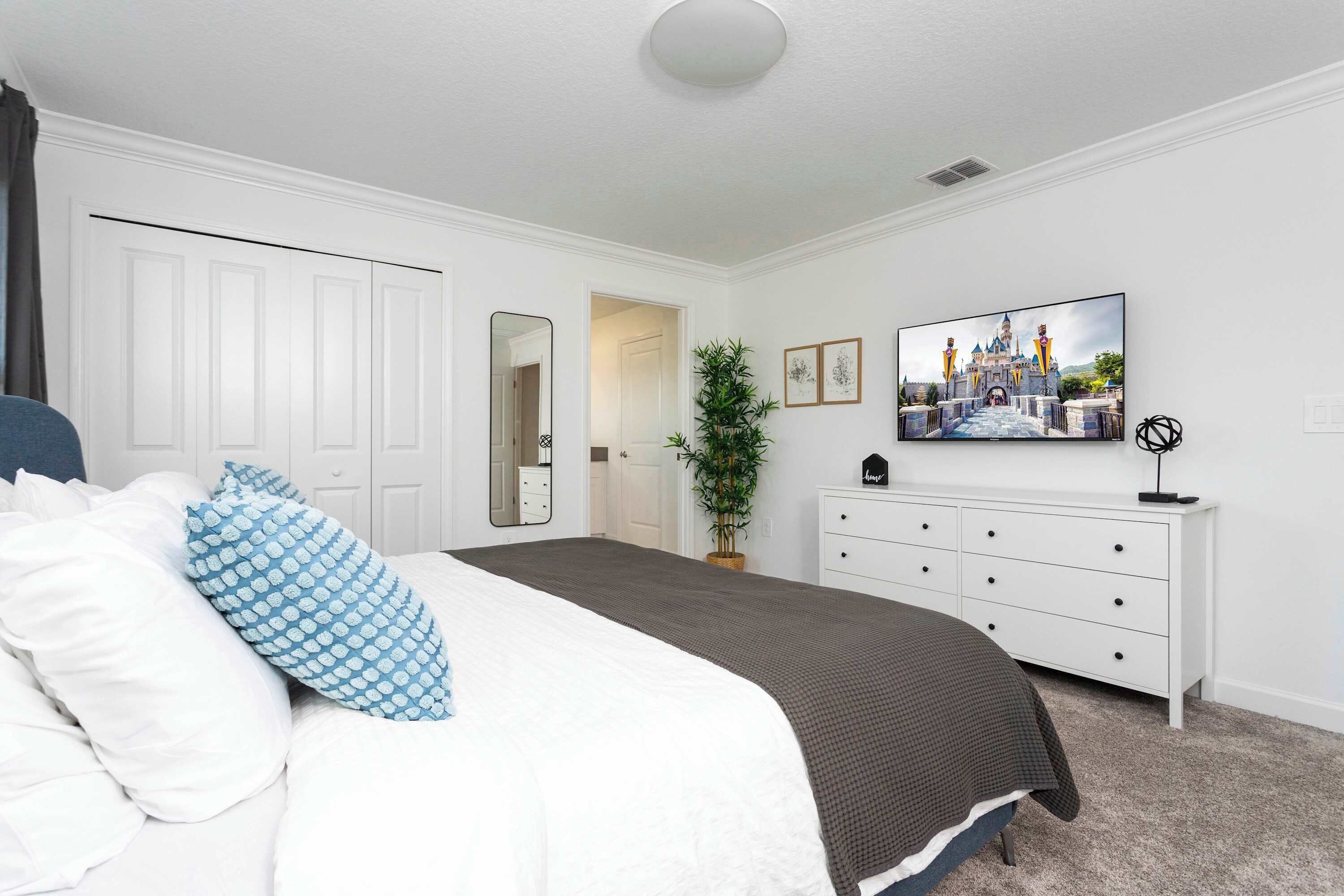 A bedroom with a bed, white dresser, and a painting of a castle.