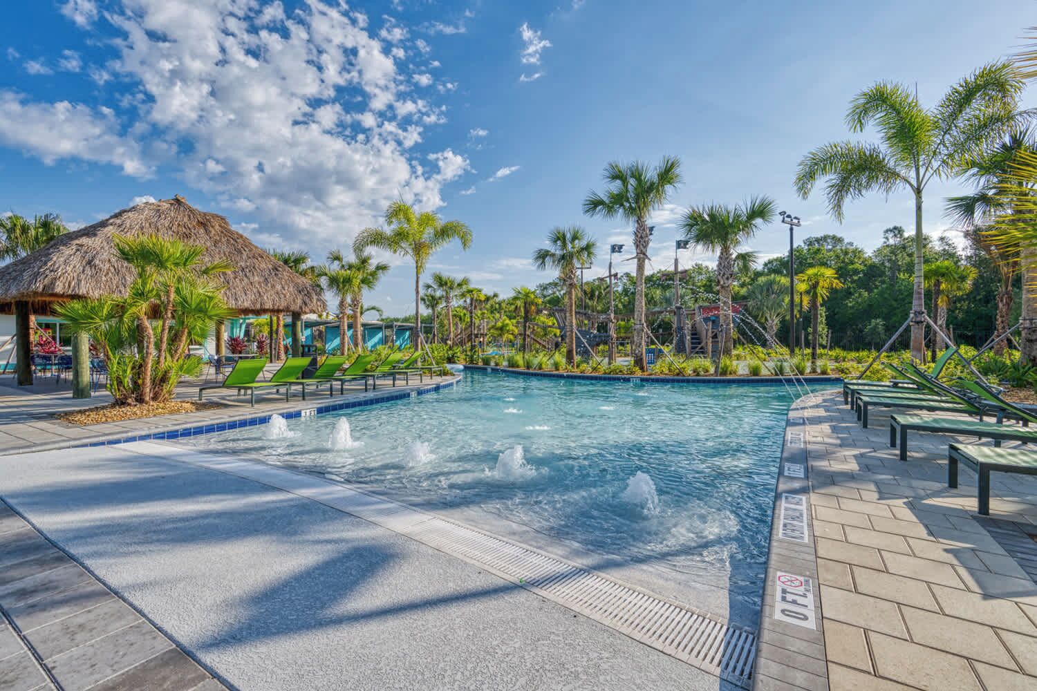 A swimming pool with a thatched-roof hut, palm trees, and lounge chairs.