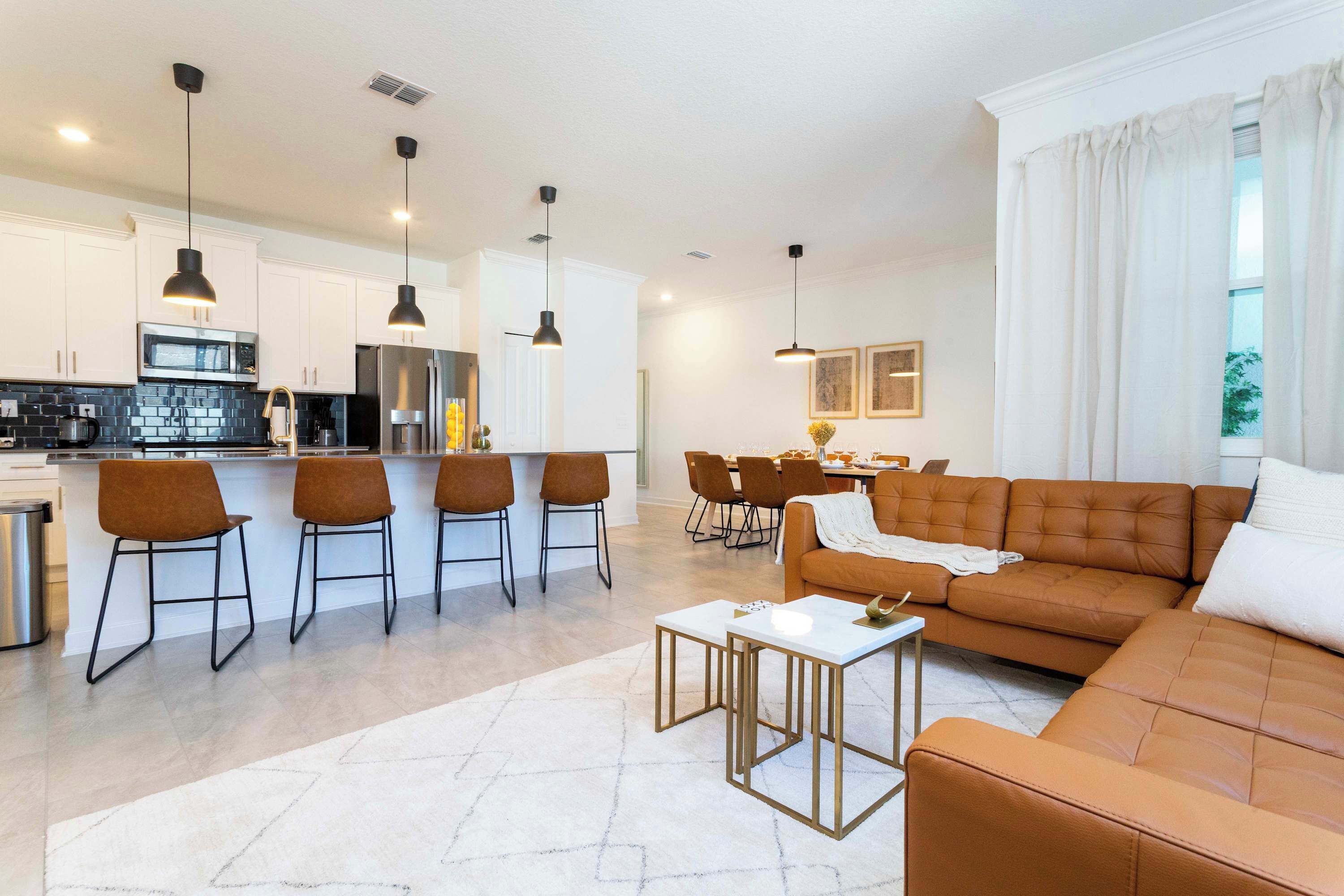A modern living room with a brown sofa, a coffee table, and a dining area with chairs and a table.