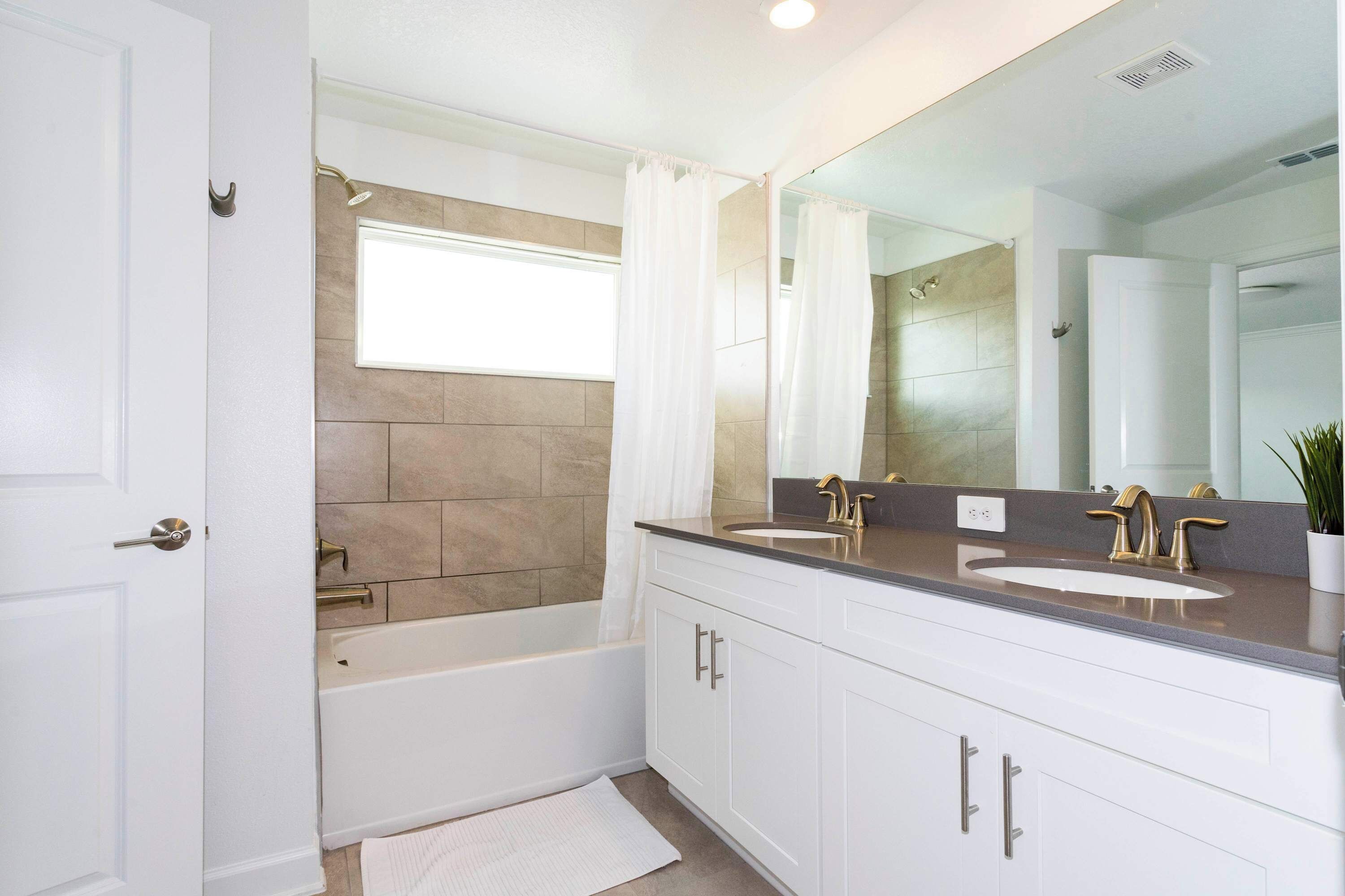 A modern bathroom with a bathtub, two sinks, and a large mirror.