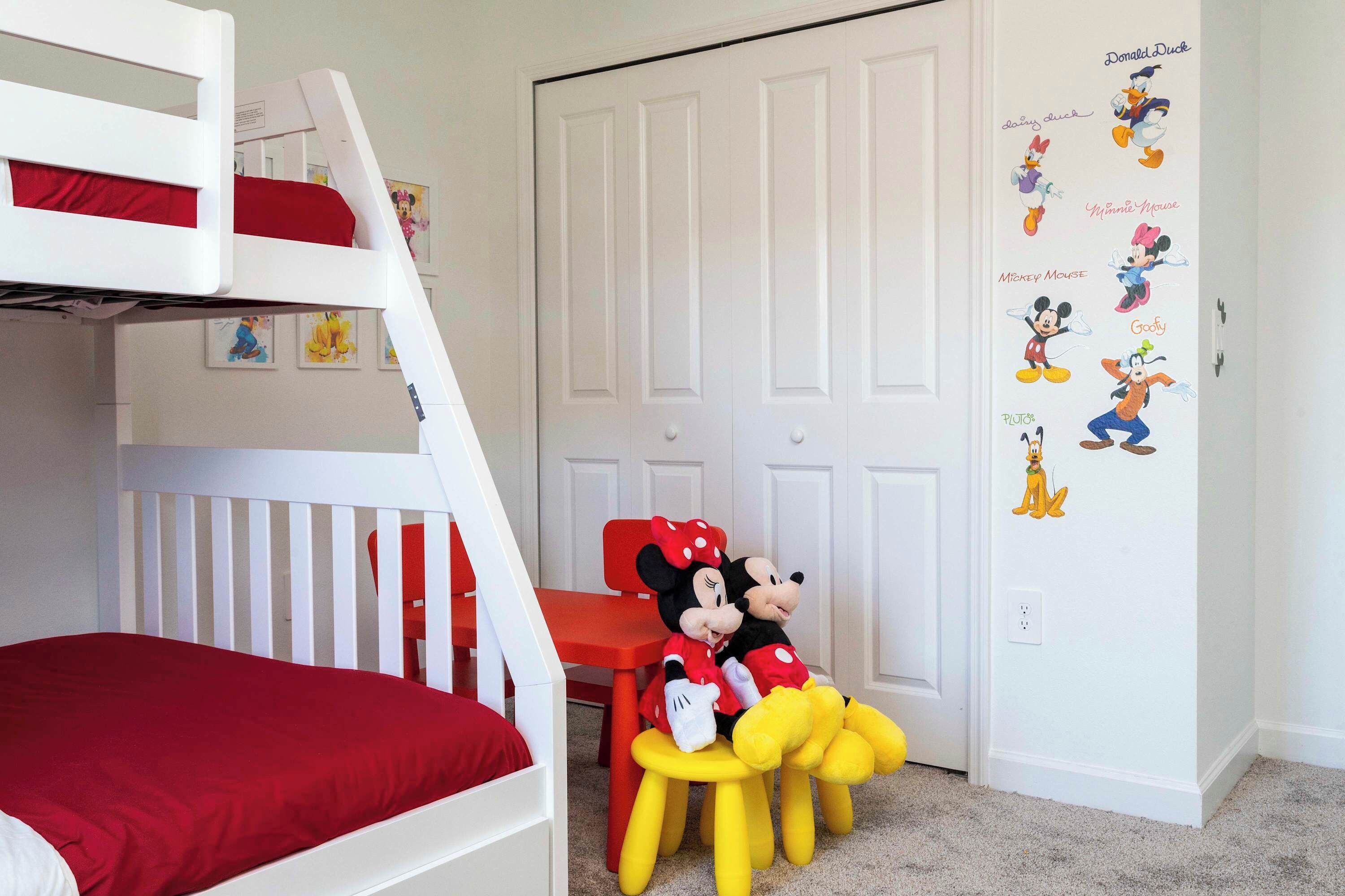 A child's room with bunk beds, a red chair, and Disney-themed wall decals.