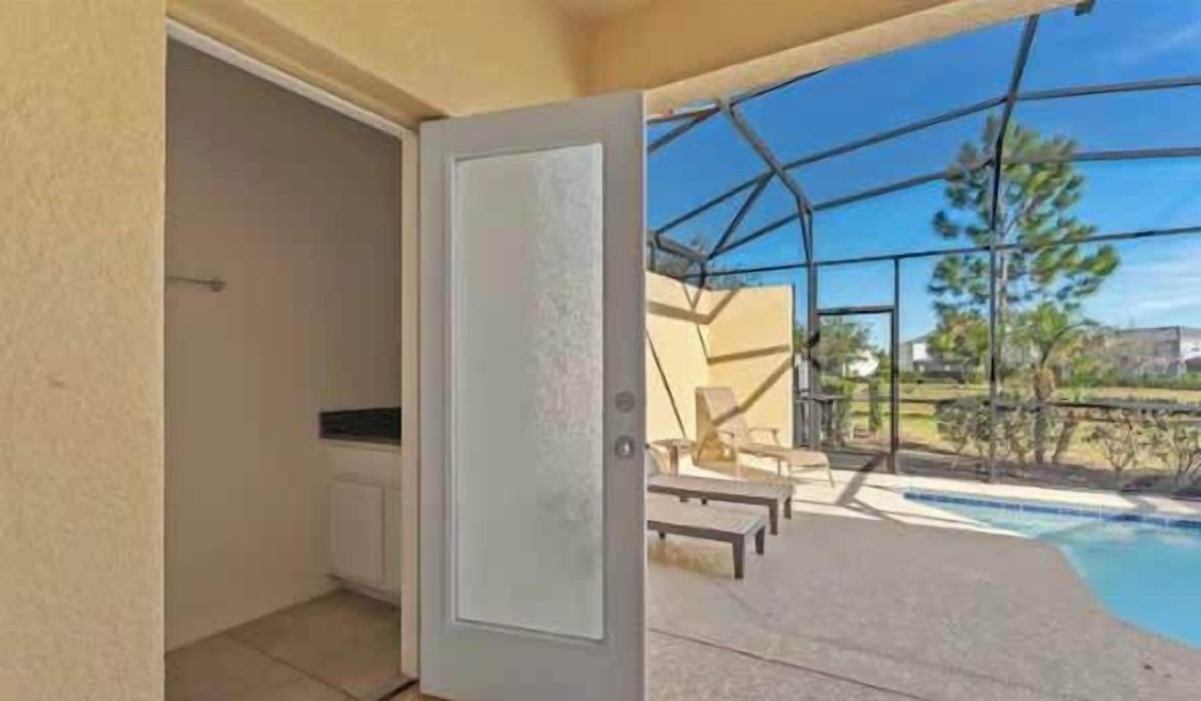 An open door leading to a balcony with a pool, outdoor furniture, and a view of the surrounding area.