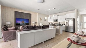 A modern living room with a sofa, a TV, and a dining area with a table set for two. - Themed Mickey Bedroom 4BR at Solterra (Davenport)