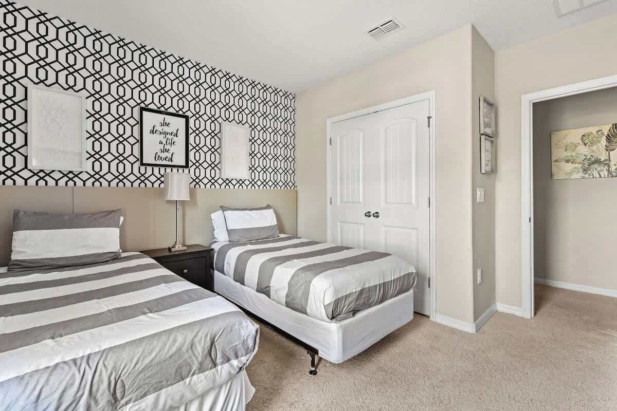 A bedroom with two beds, a geometric-patterned wall, a white door, and a framed quote.