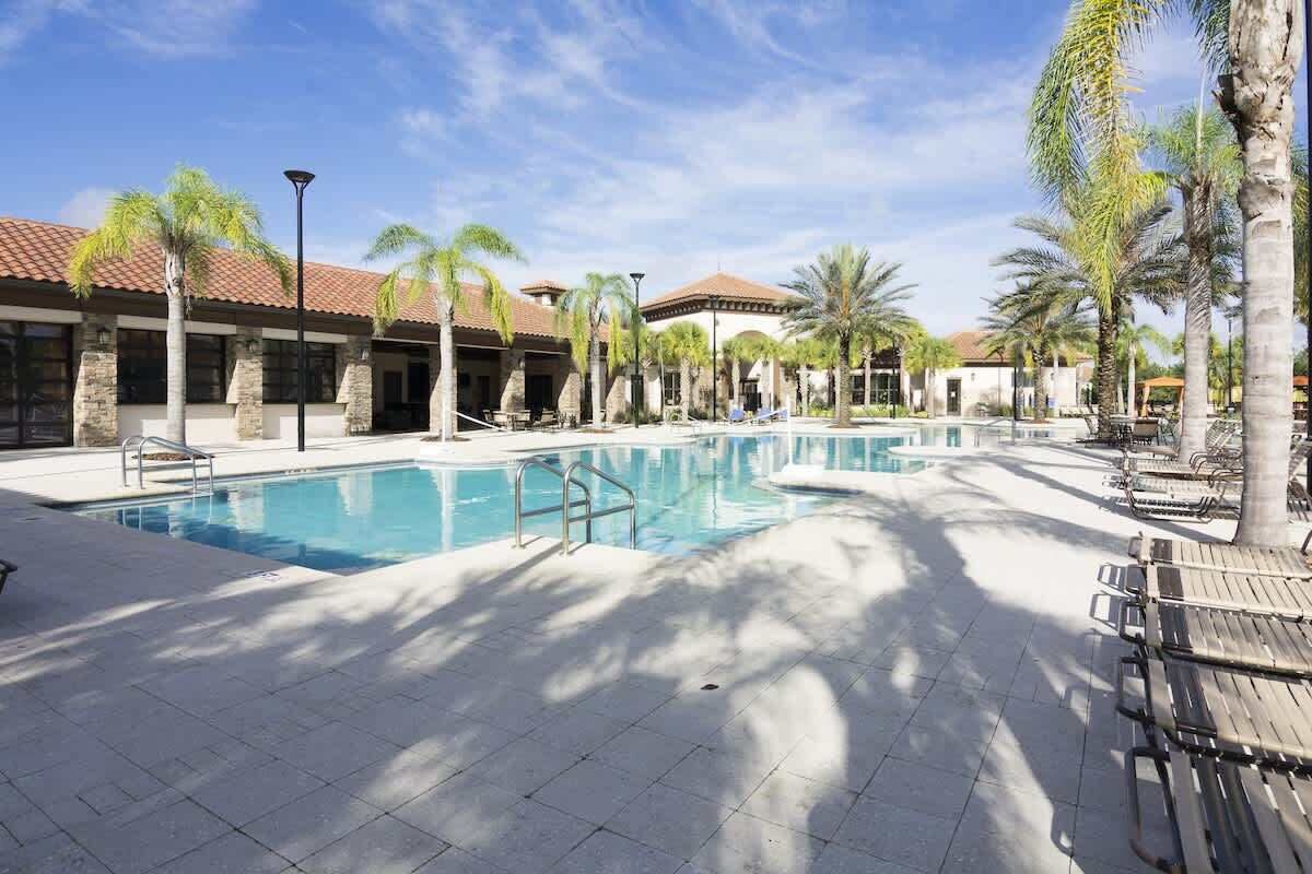Une piscine entourée de chaises longues et de palmiers, le tout bordé de bâtiments aux toits recouverts de tuiles.