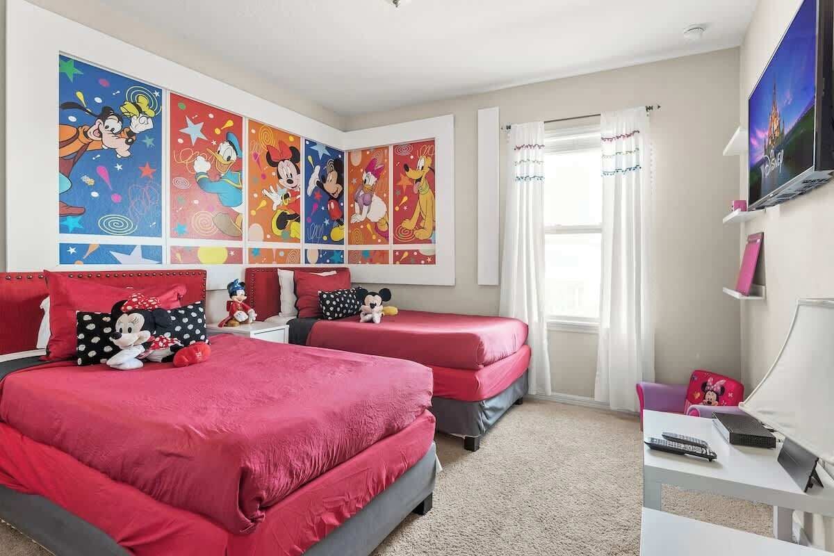 Quarto com duas camas, televisão e escrivaninha.