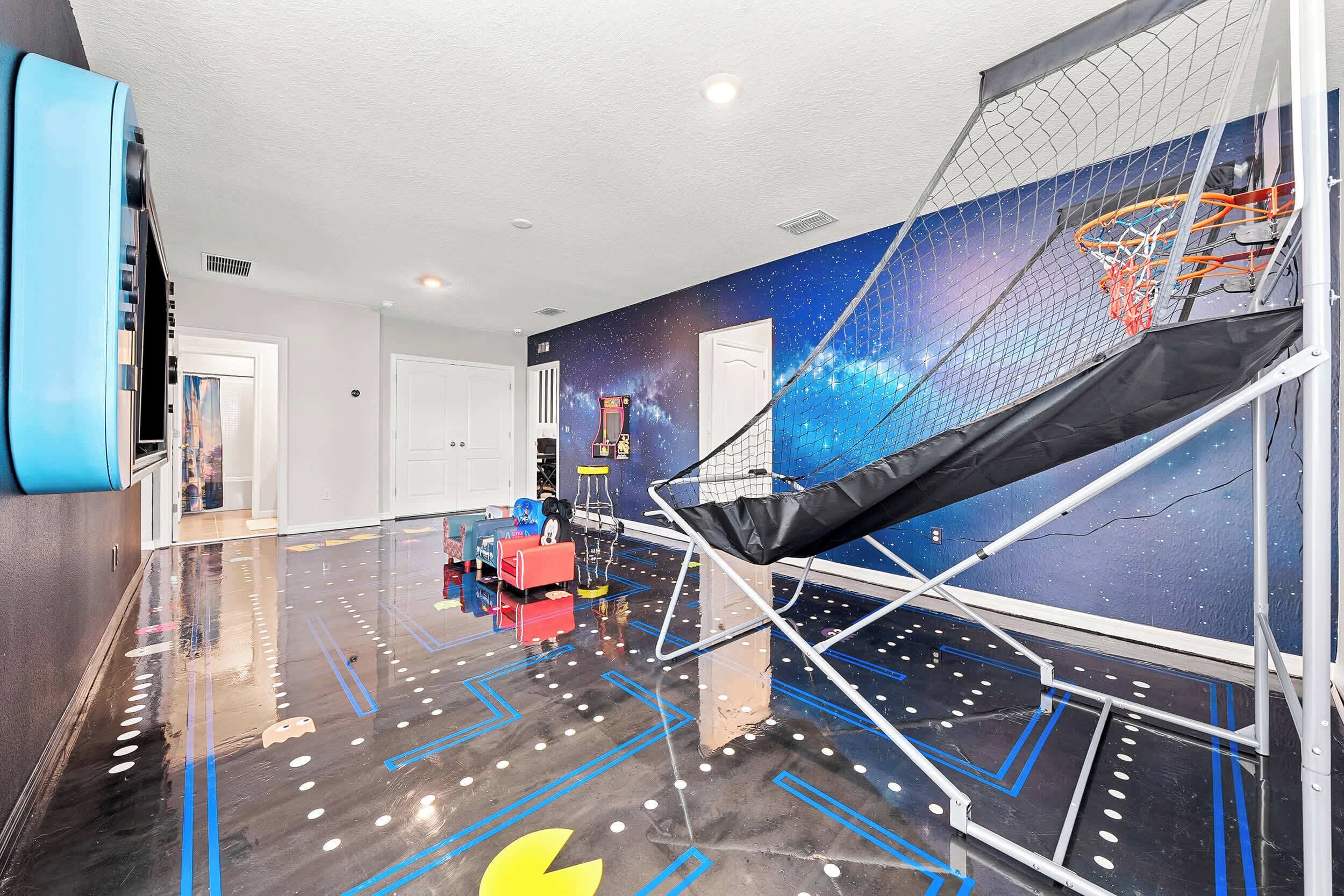 A spacious room with a basketball hoop, a trampoline, and a space-themed mural on the wall.