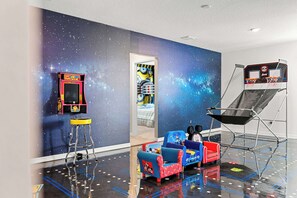 Una habitación con un mural con temática espacial, un pequeño aro de baloncesto y sillas coloridas.
