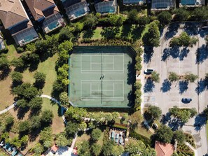Vista aérea de una zona residencial con canchas de tenis rodeadas de árboles y casas.