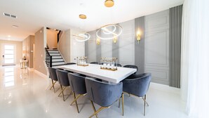 A modern dining area with a white table, dark chairs, and a staircase in the background. - Themed 9BR Retreat, Pool & Soccer Fun (Kissimmee)
