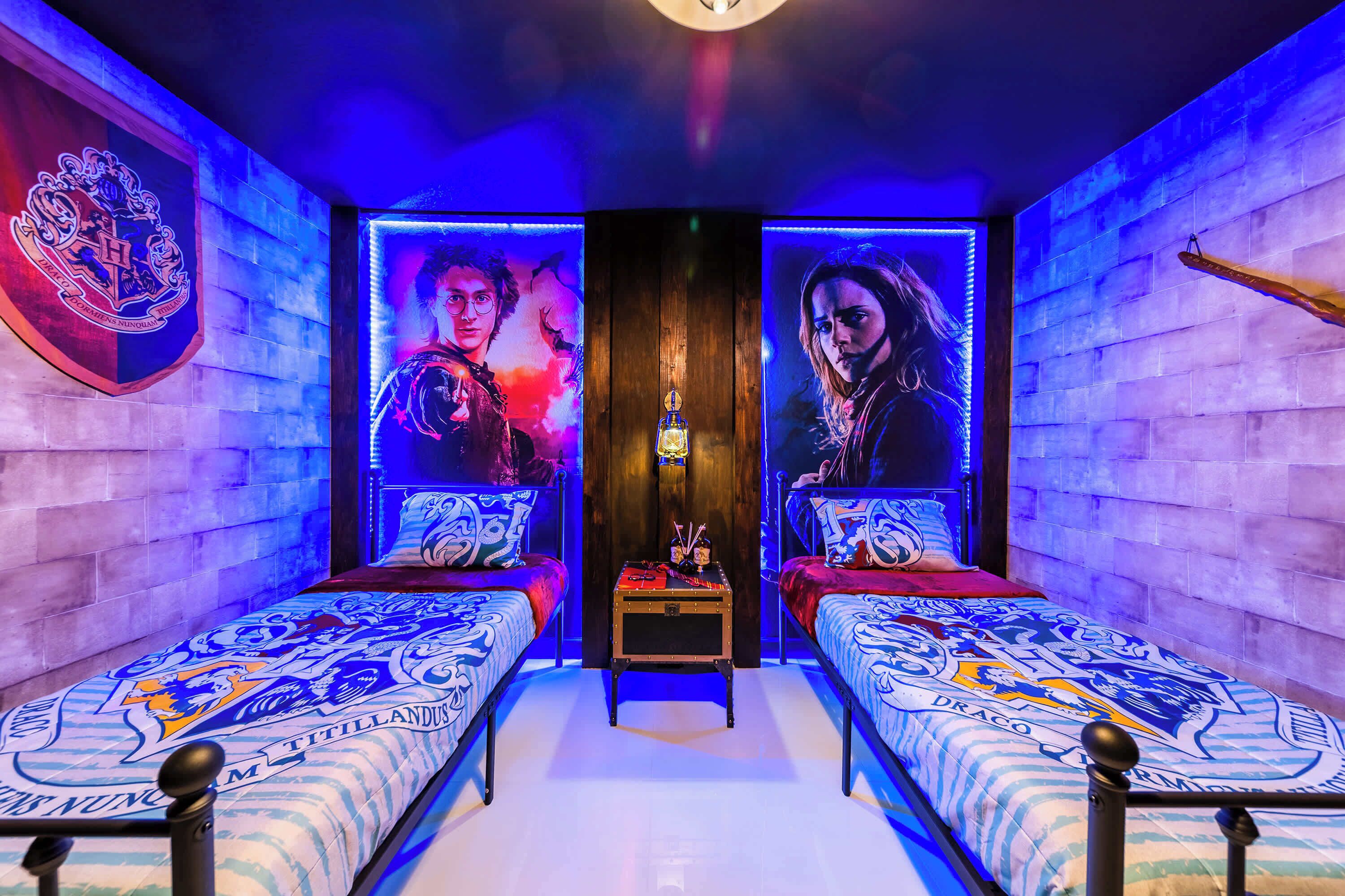 A room with two beds, a small table, and a wall with a crest and portraits.