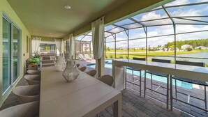 A covered patio with a pool, outdoor seating, and a view of a golf course. - Themed 9BR Retreat, Pool & Soccer Fun (Kissimmee)