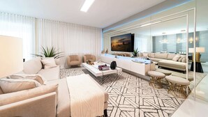 A modern living room with a sofa, armchairs, a coffee table, and a TV. - Themed 9BR Retreat, Pool & Soccer Fun (Kissimmee)