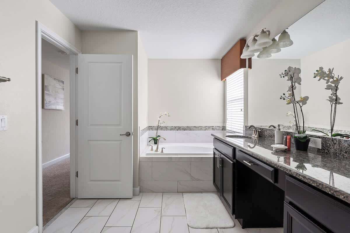 A modern bathroom with a white door, a bathtub, a sink, and a countertop with decorative plants.