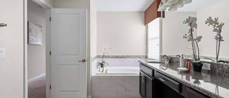 A modern bathroom with a white door, a bathtub, a sink, and a countertop with decorative plants.