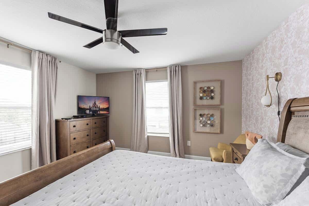 A bedroom with a bed, a ceiling fan, a dresser, a TV, and artwork on the walls.