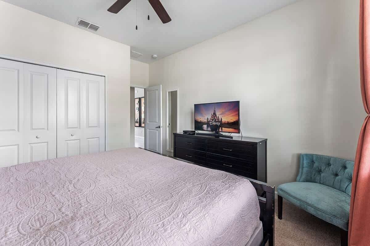 Une chambre avec un grand lit, un téléviseur posé sur une commode, un fauteuil turquoise et un tableau accroché au mur.