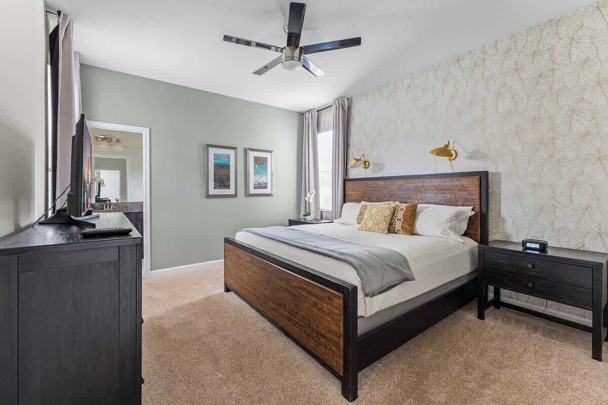 Une chambre à coucher comprenant un lit, des tables de chevet, une commode, un ventilateur de plafond et des tableaux encadrés accrochés au mur.