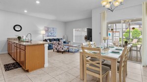 A modern kitchen with a central island, dining area with wooden chairs, and a large window with blinds. - Townhome 4BR With Pool at Storey Lake (Kissimmee)