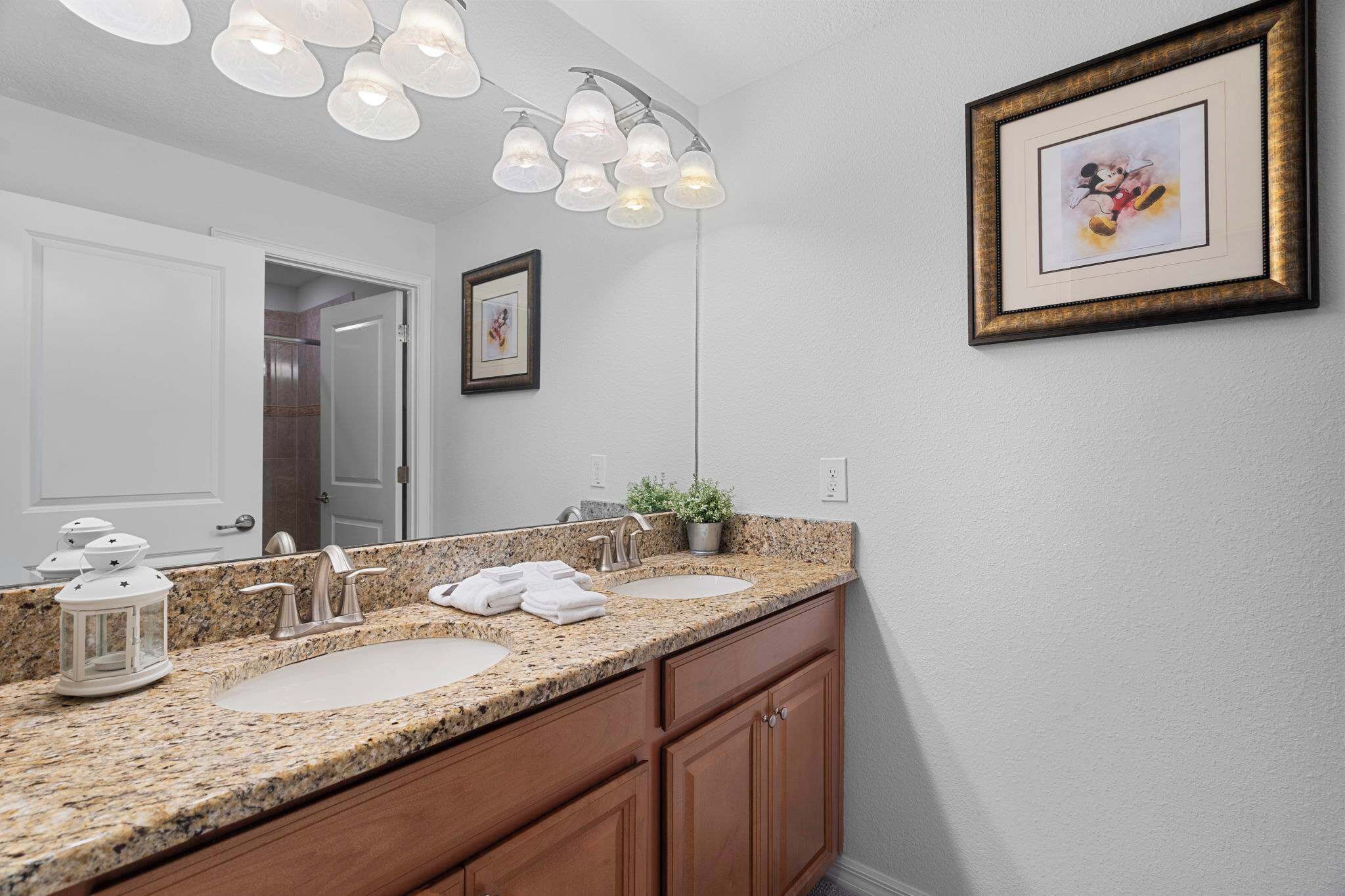 Une salle de bain avec un comptoir en granit, deux lavabos, un miroir et un luminaire au plafond.