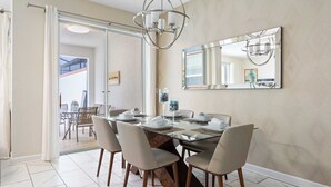 Comedor con mesa de vidrio, sillas, lámpara de araña y un espejo grande en la pared.