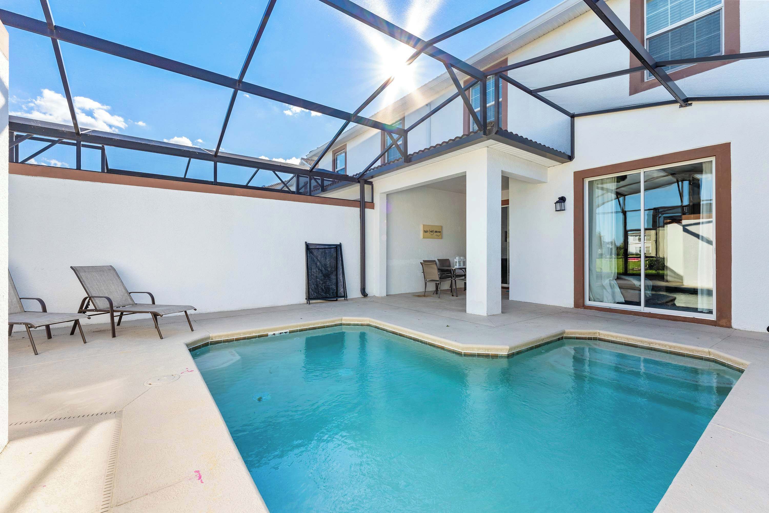 A pool area with a glass enclosure, lounge chairs, and a patio table.