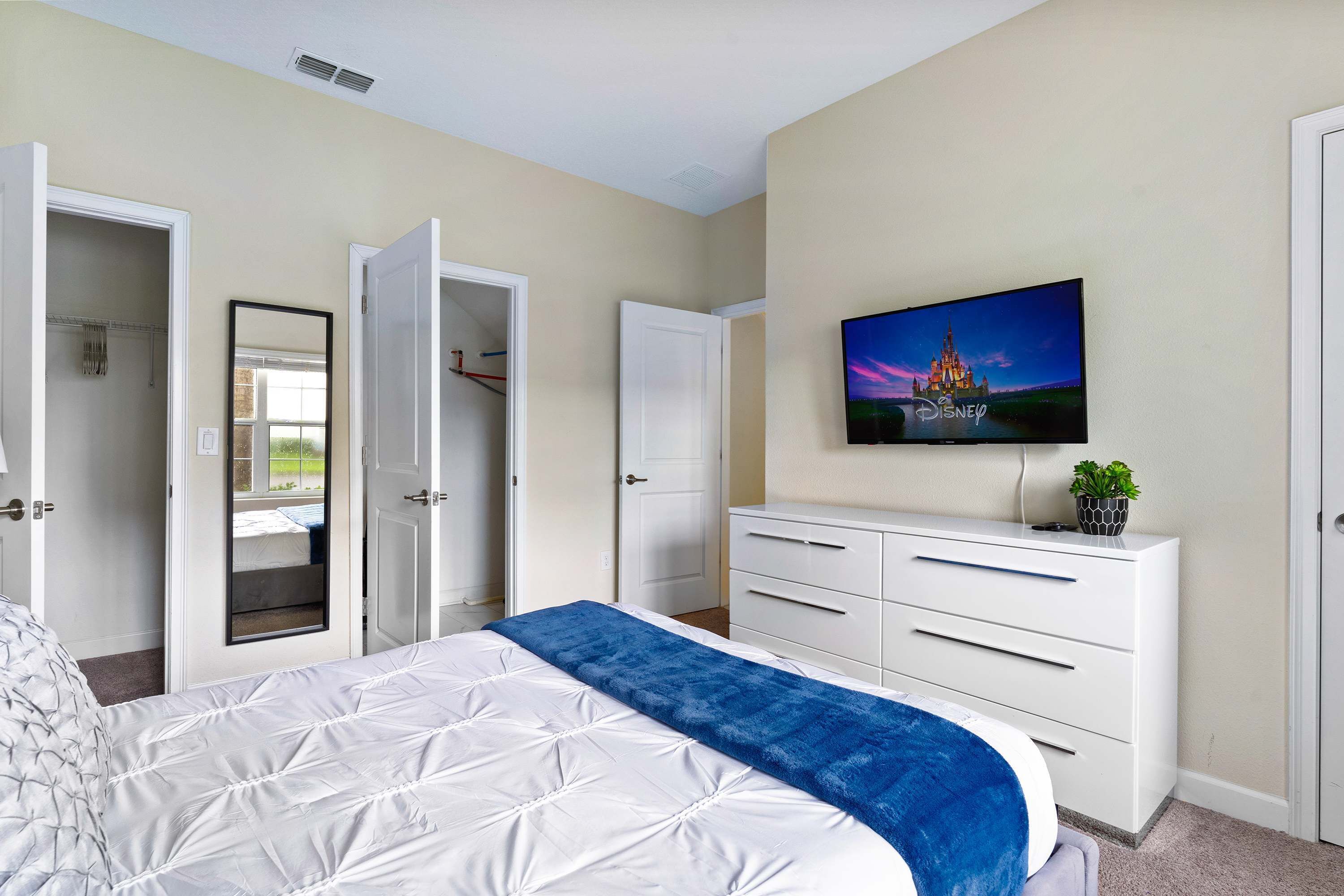 A bedroom with a bed, a dresser, a television, and an open closet.