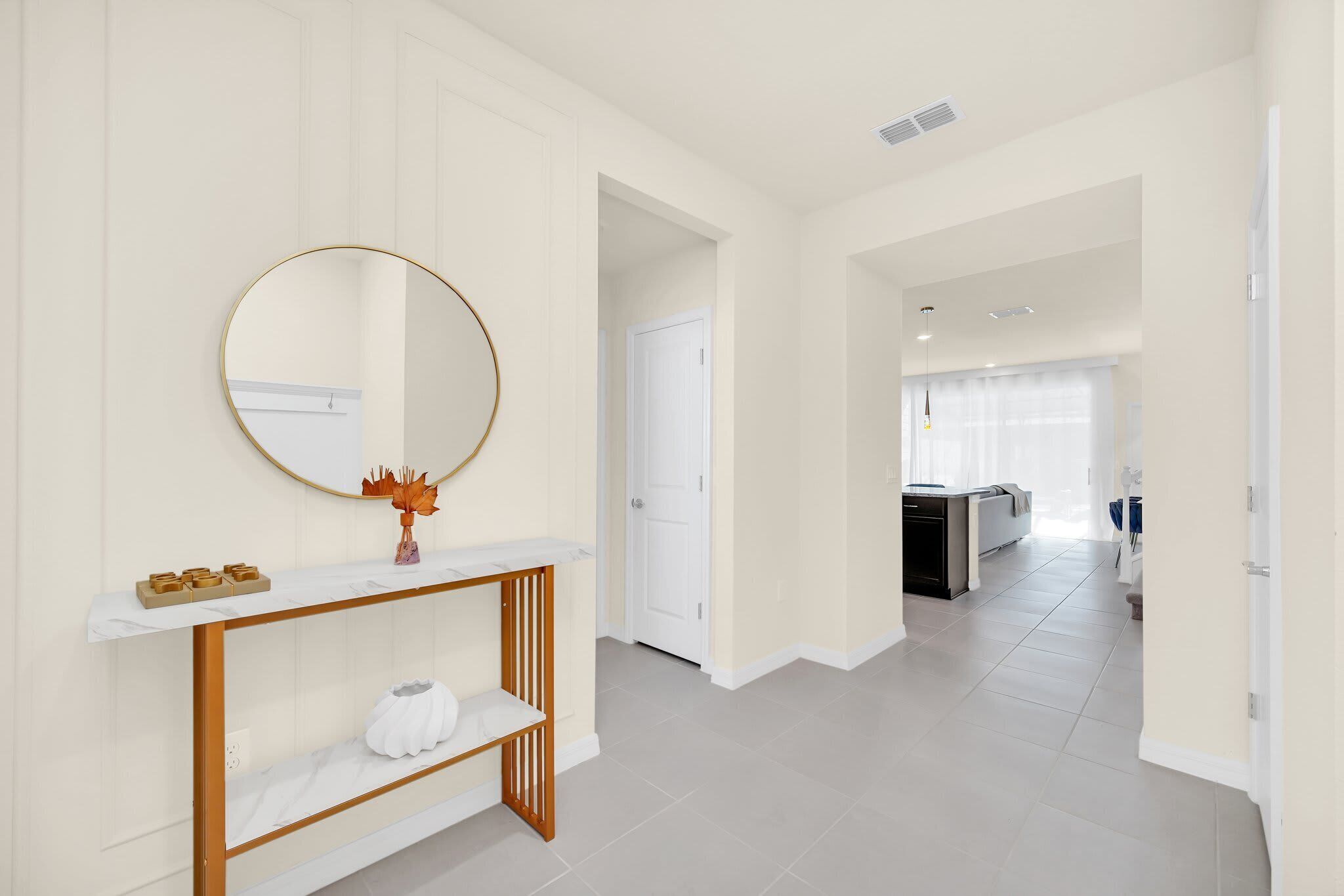 A hallway with a white console table, a round mirror, and a door leading to a kitchen area.
