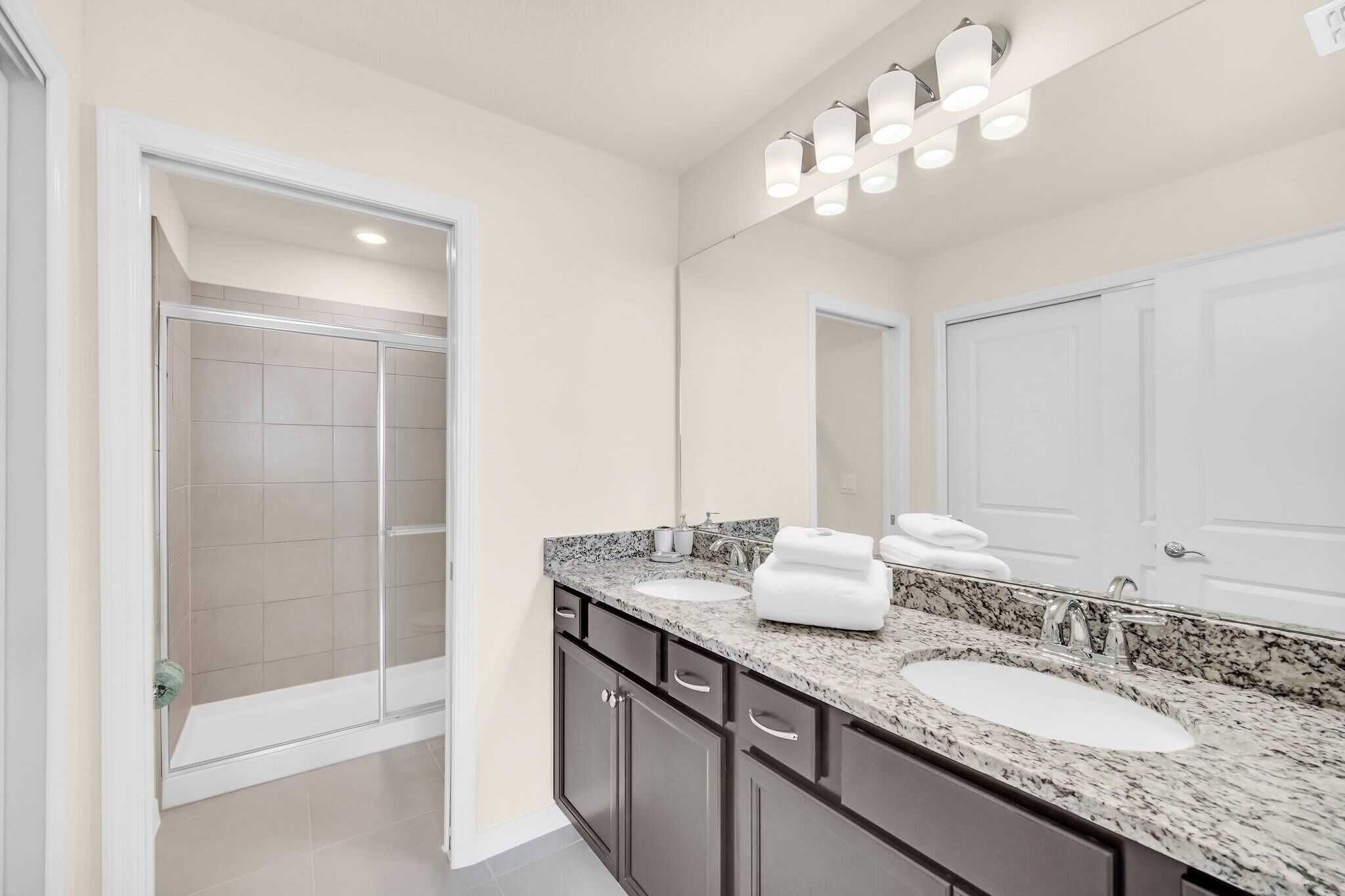 A modern bathroom with a double sink, a glass shower enclosure, and a large mirror.
