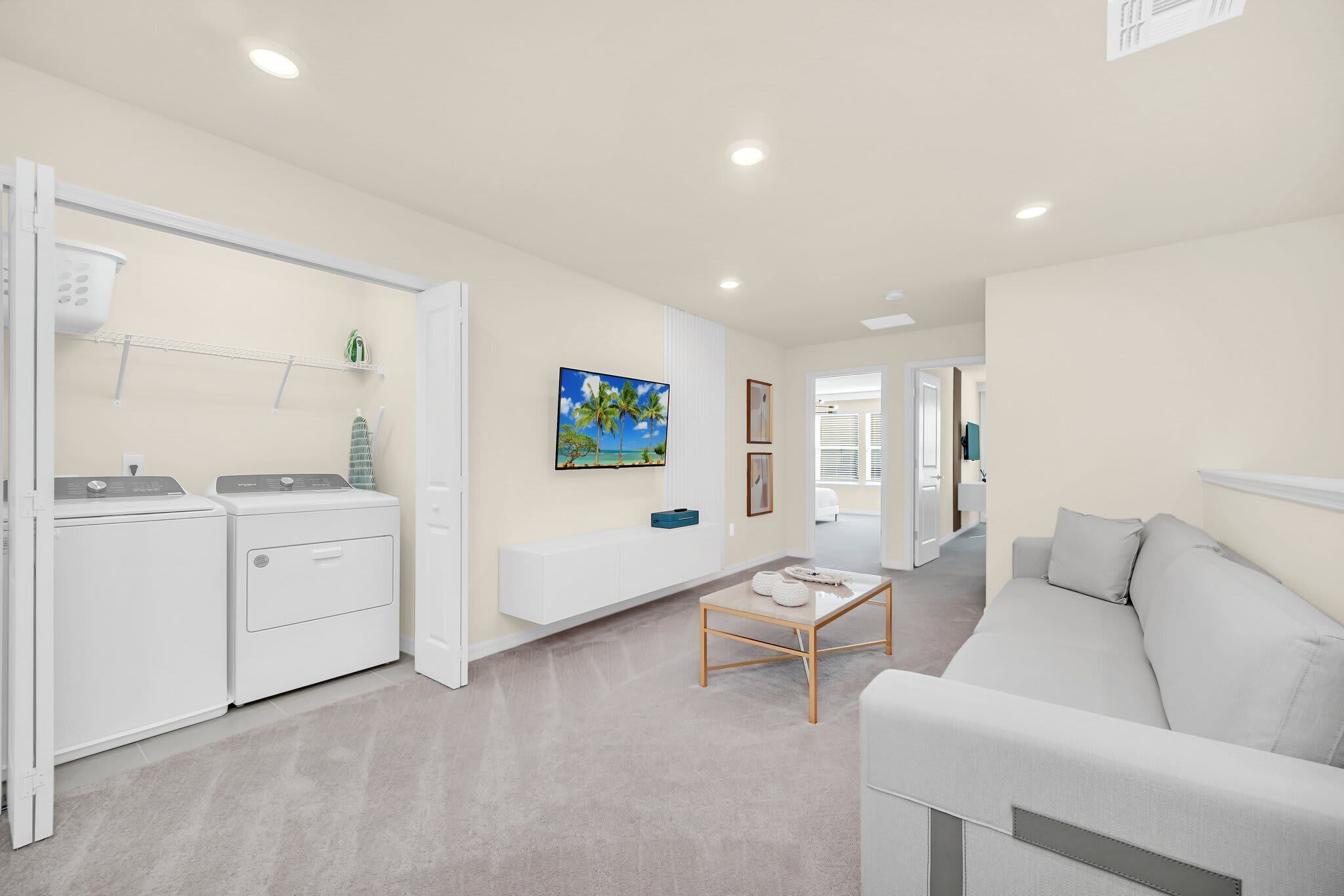 A modern living room with a grey sofa, a coffee table, and a laundry area with two washing machines.