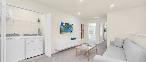 A modern living room with a grey sofa, a coffee table, and a laundry area with two washing machines.