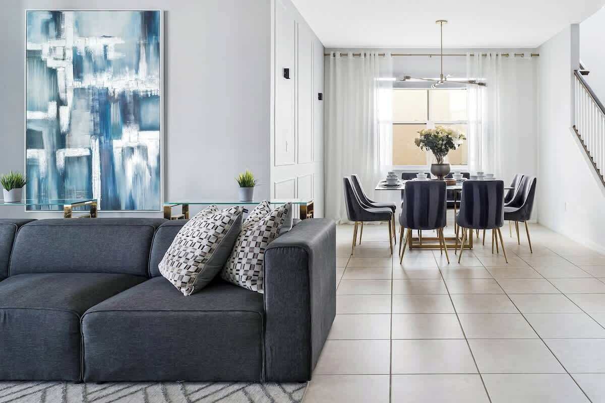 A modern living room with a gray sofa, a dining area with a table and chairs, and a large abstract painting on the wall.