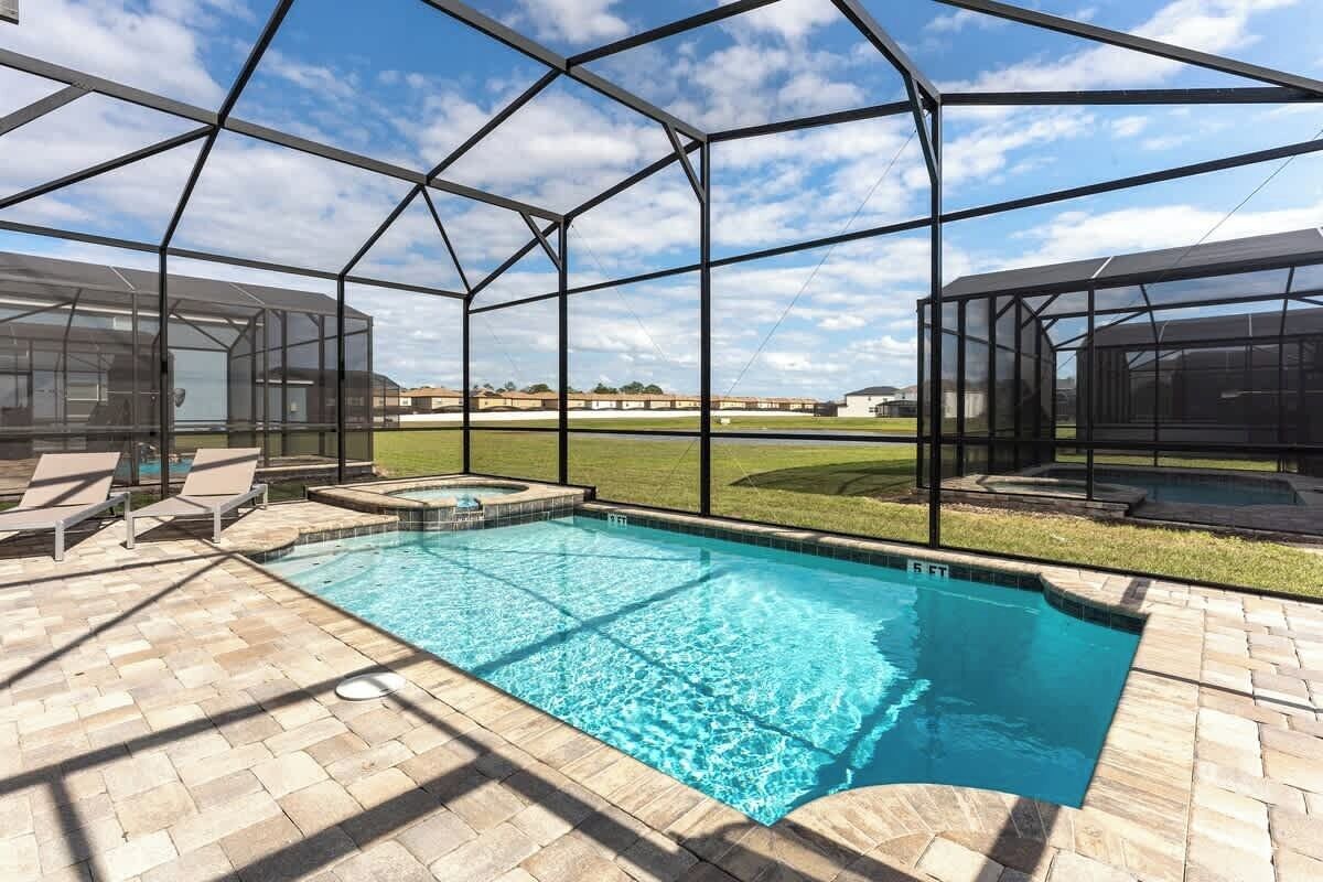A swimming pool with a clear blue water, surrounded by a covered patio area with lounge chairs and a hot tub.