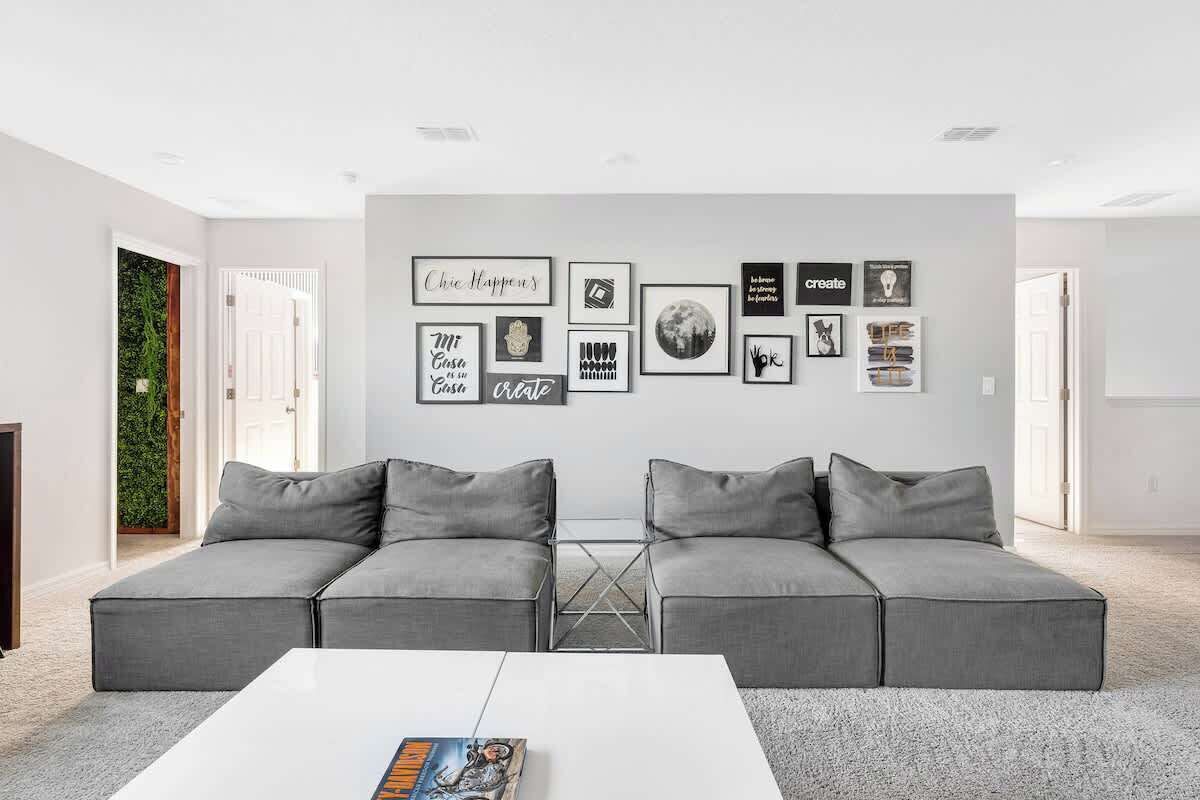 A modern living room with a grey sectional sofa, a white coffee table, and a wall decorated with various framed artworks.