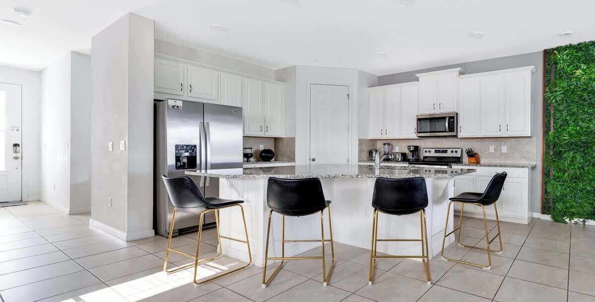 A modern kitchen with white cabinets, a stainless steel refrigerator, a microwave, and a built-in island with bar stools.