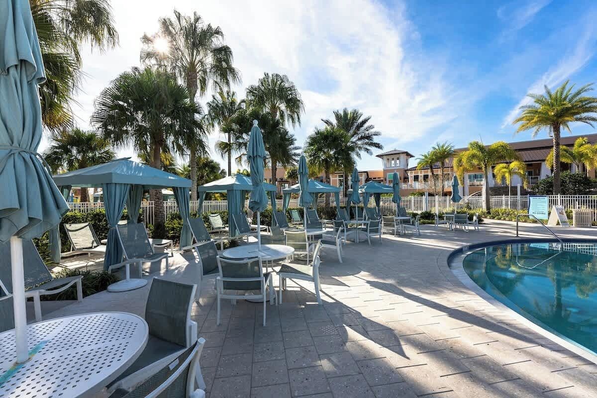 A poolside area with lounge chairs and umbrellas, a pool, and palm trees.