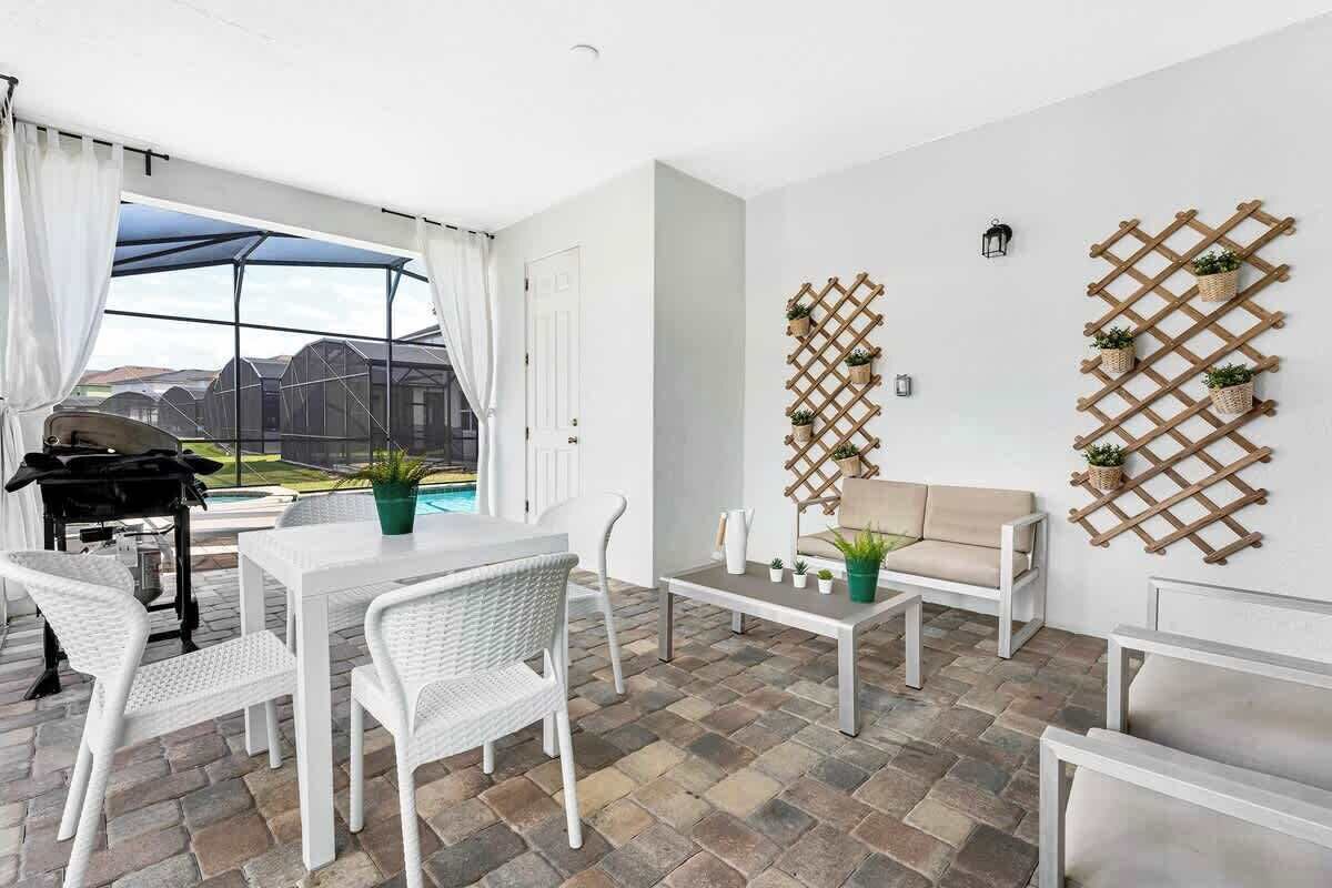 A patio area with a white table and chairs, a beige sofa, and a wooden lattice wall with potted plants.